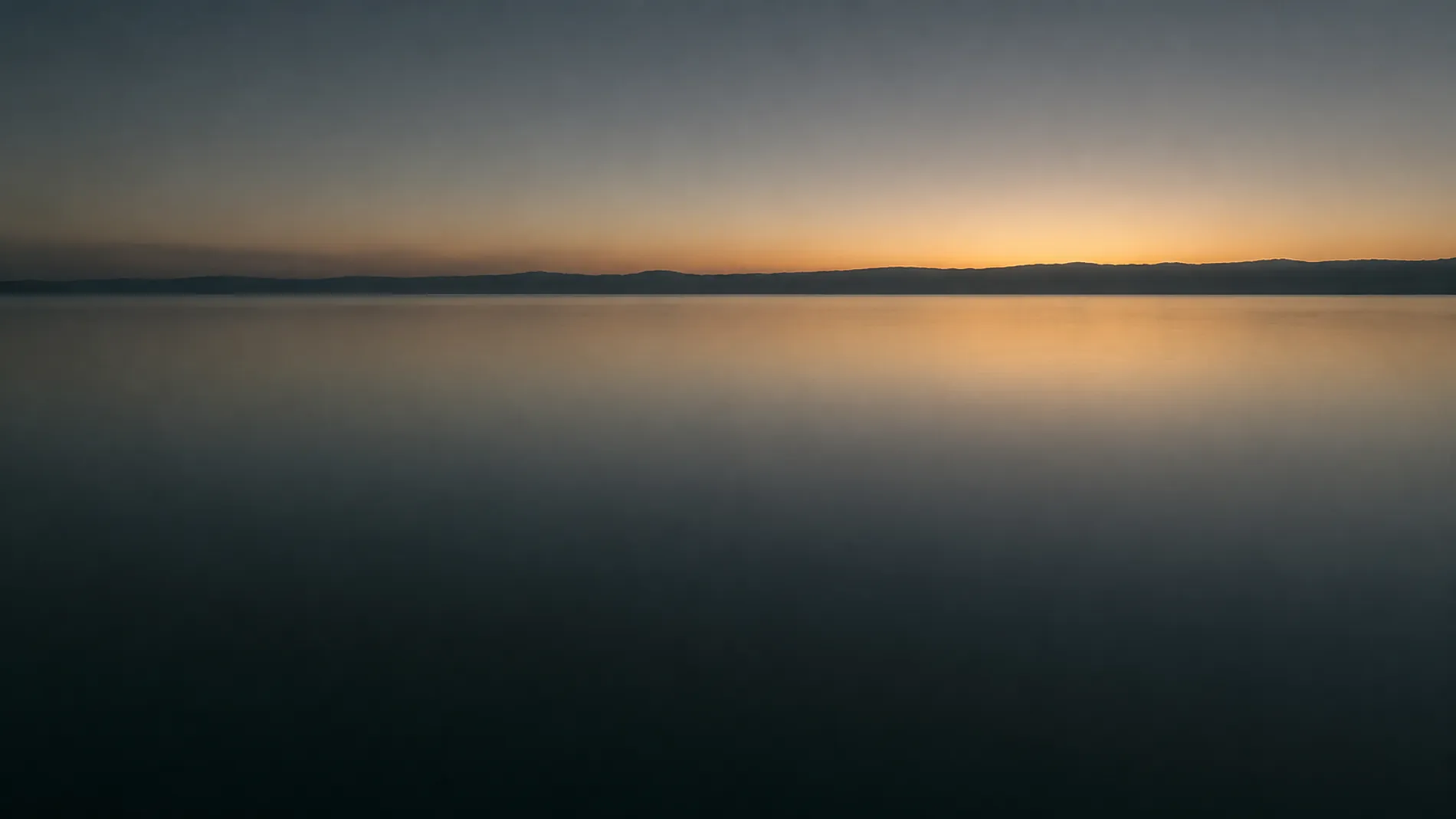 Still water meeting a soft dusk sky, with one low distant ridge along the horizon.